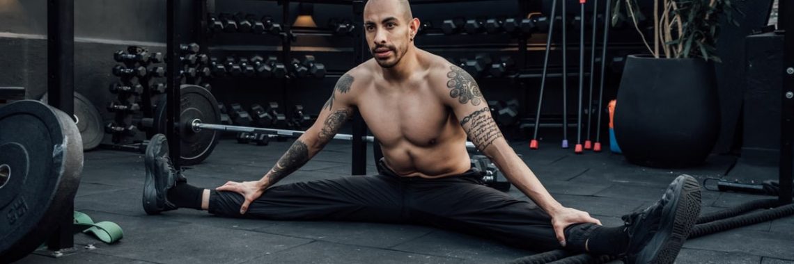 Tattooed man performing a split stretch in a gym, showcasing flexibility and fitness lifestyle in Mexico City.